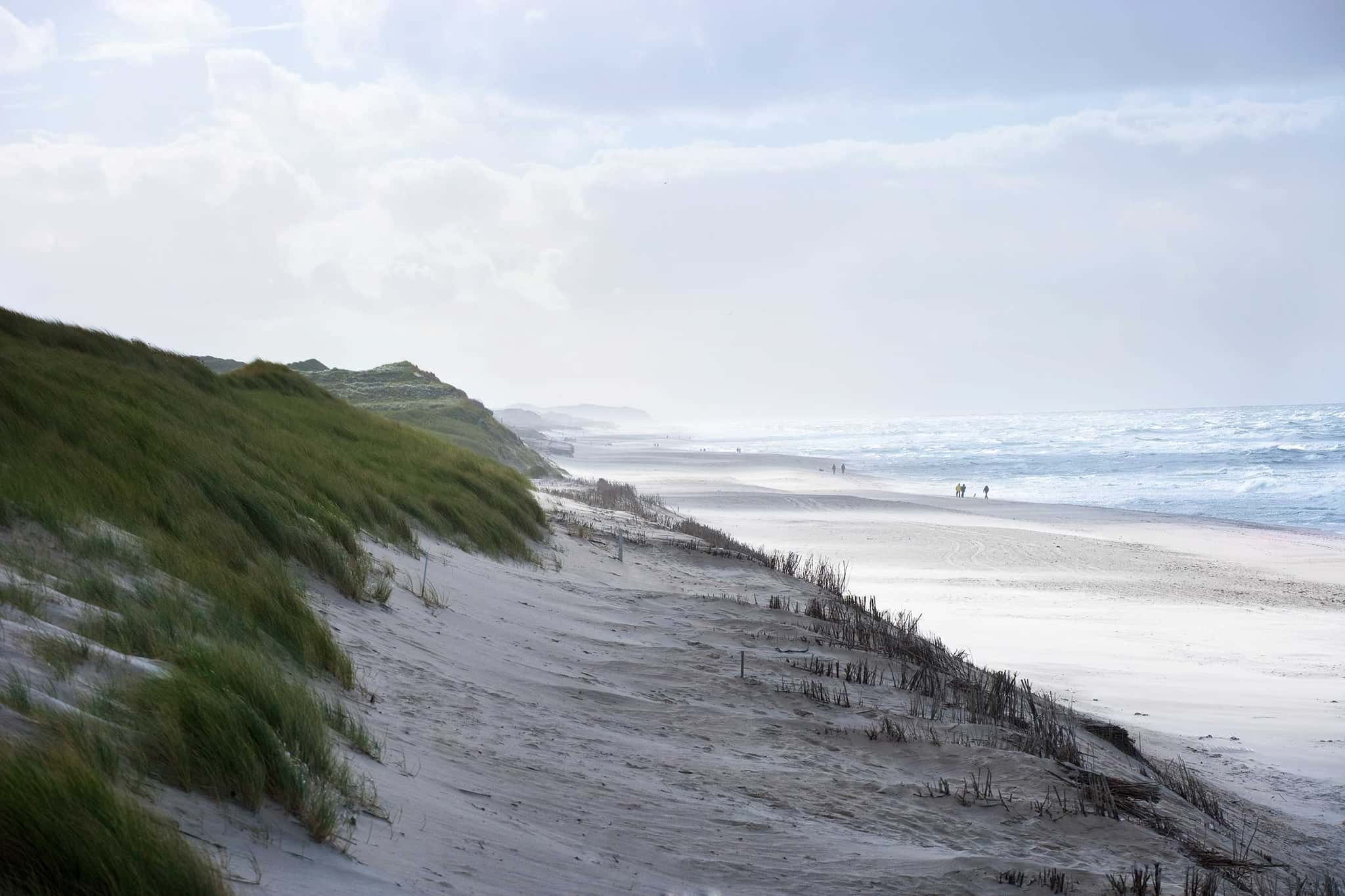 Breiter Sandstrand mit Brandung und begrünten Dünen an einem windigen Tag auf Sylt