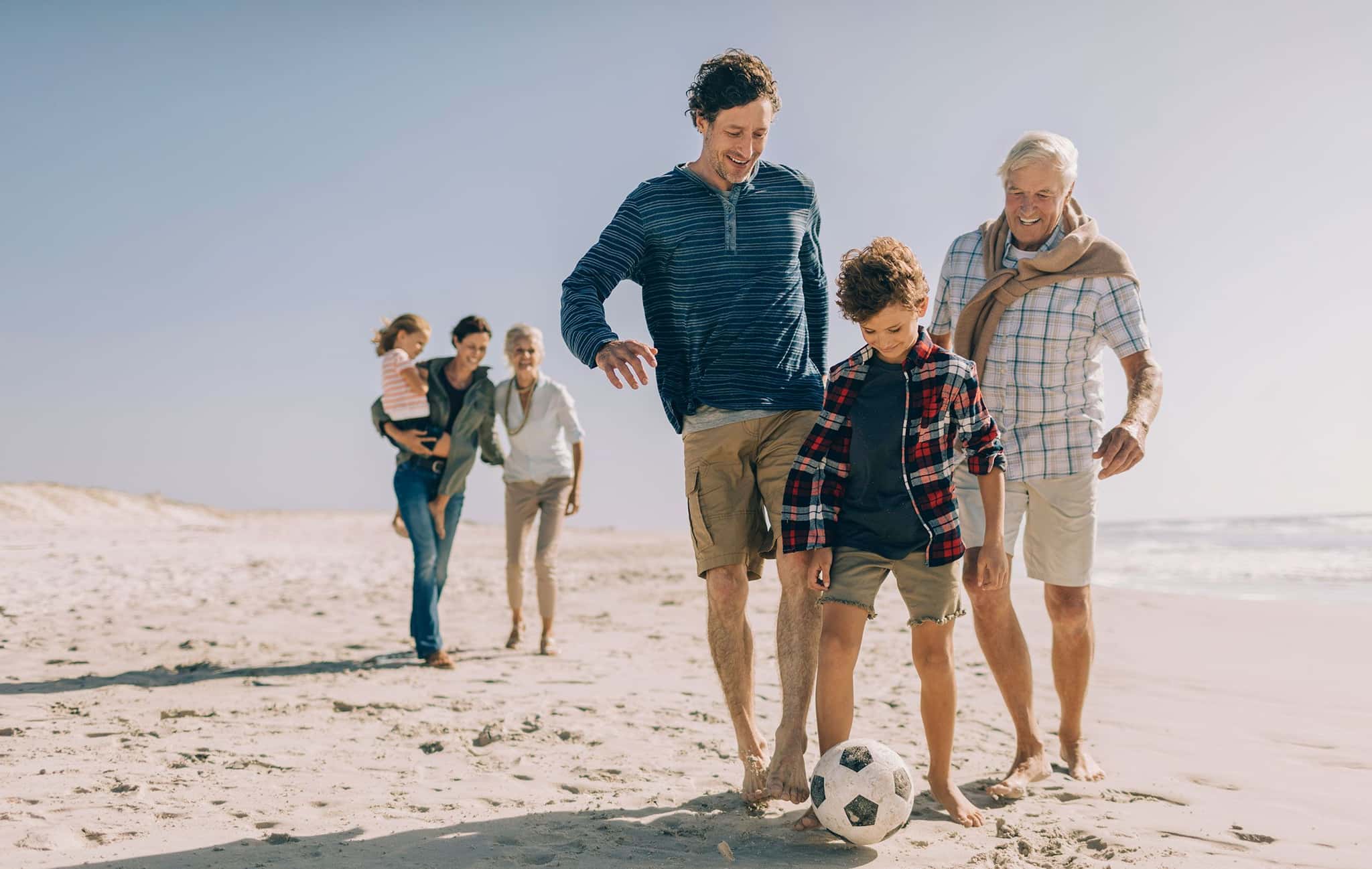 Drei Generationen einer Familie spielen am Sandstrand Fußball