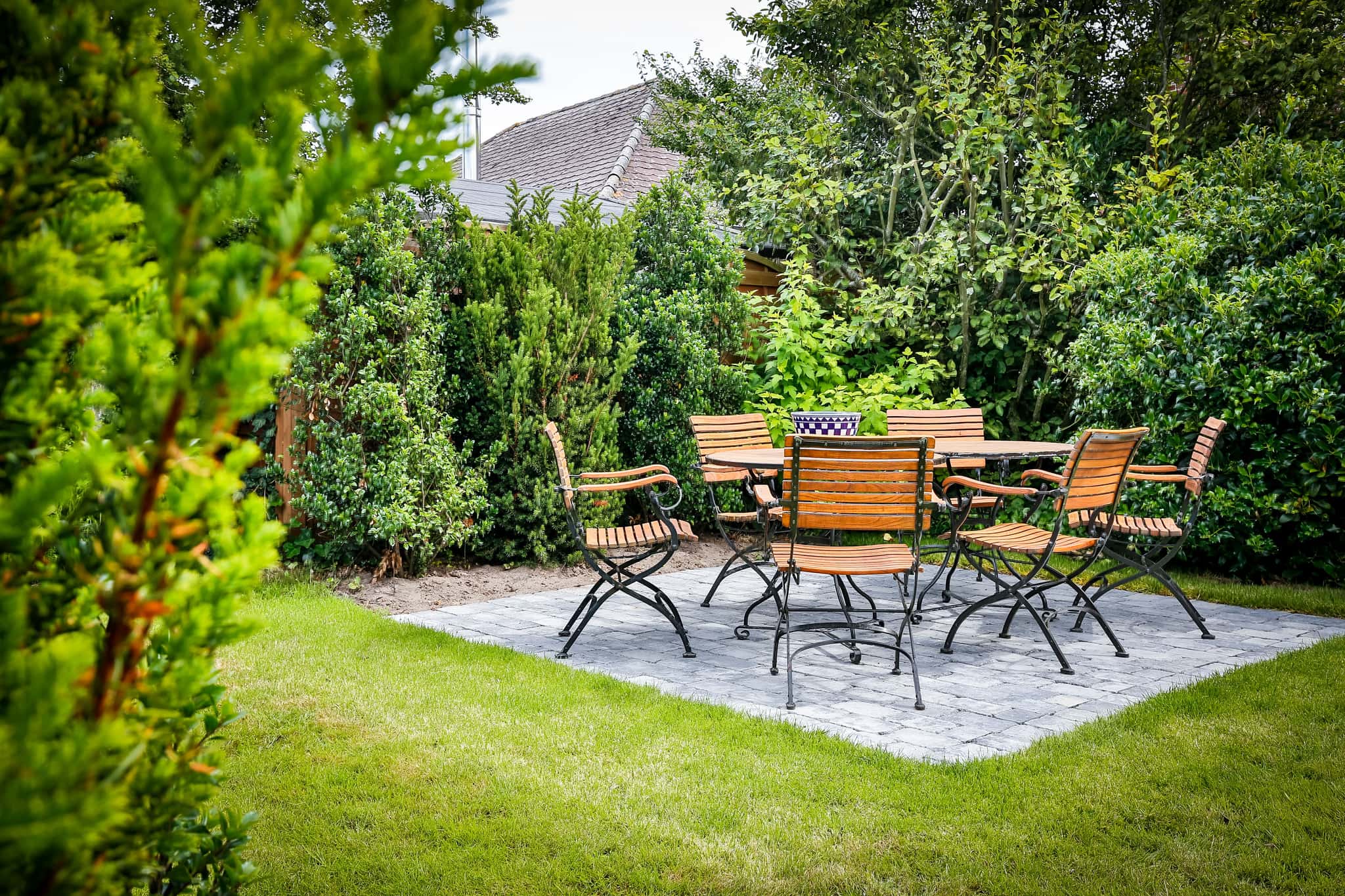 Gartenterrasse mit Holzklappstühlen und rundem Tisch, umgeben von Hecken und Rasen beim Fährhüs