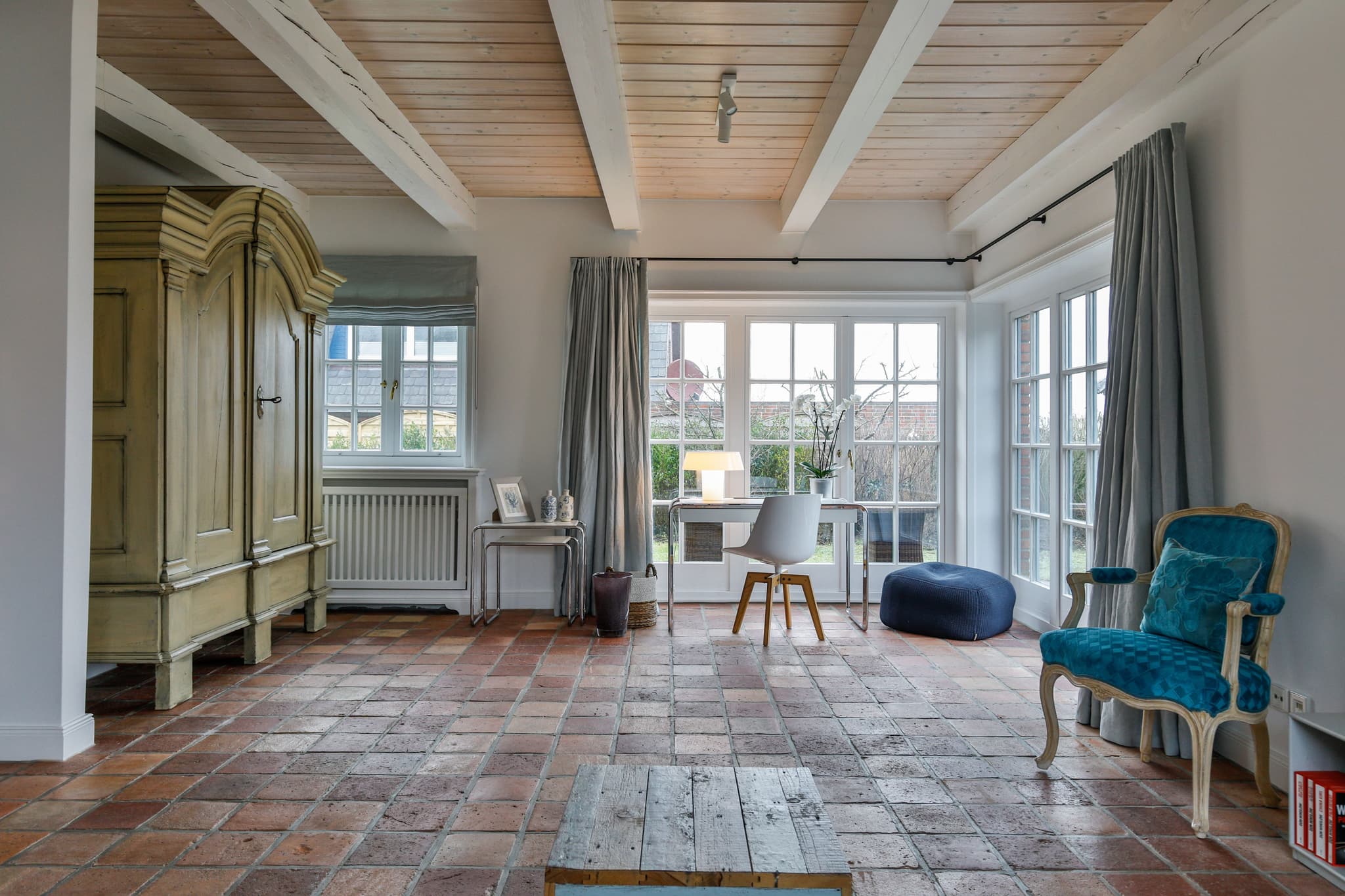 Wohnbereich mit Terrakottaboden, Holzbalkendecke, altem Schrank und Polstersessel im Haus Lochterbarig