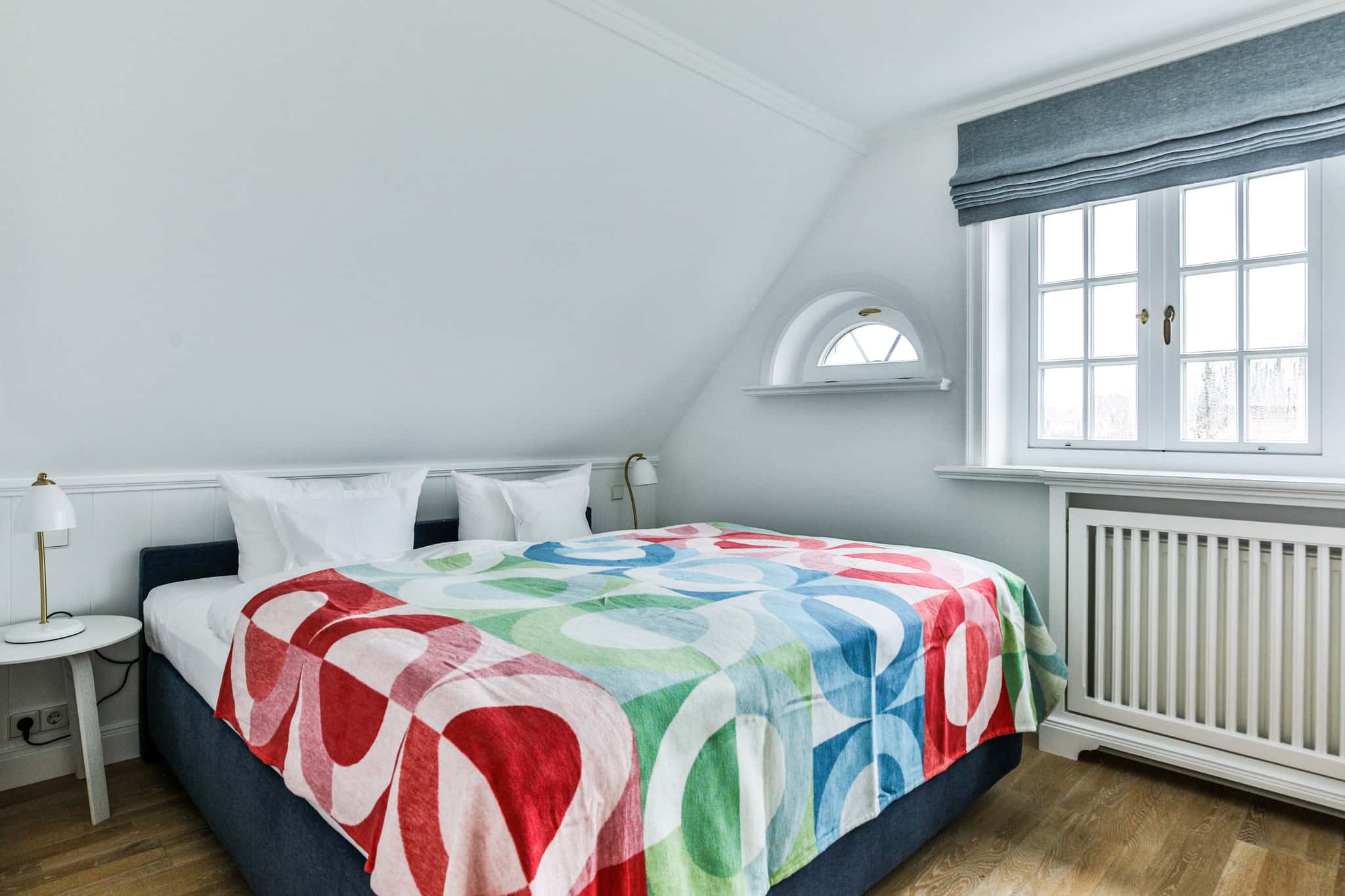Schlafzimmer mit Doppelbett, bunter Tagesdecke, Rundbogenfenster und Dachschräge im Haus Lochterbarig