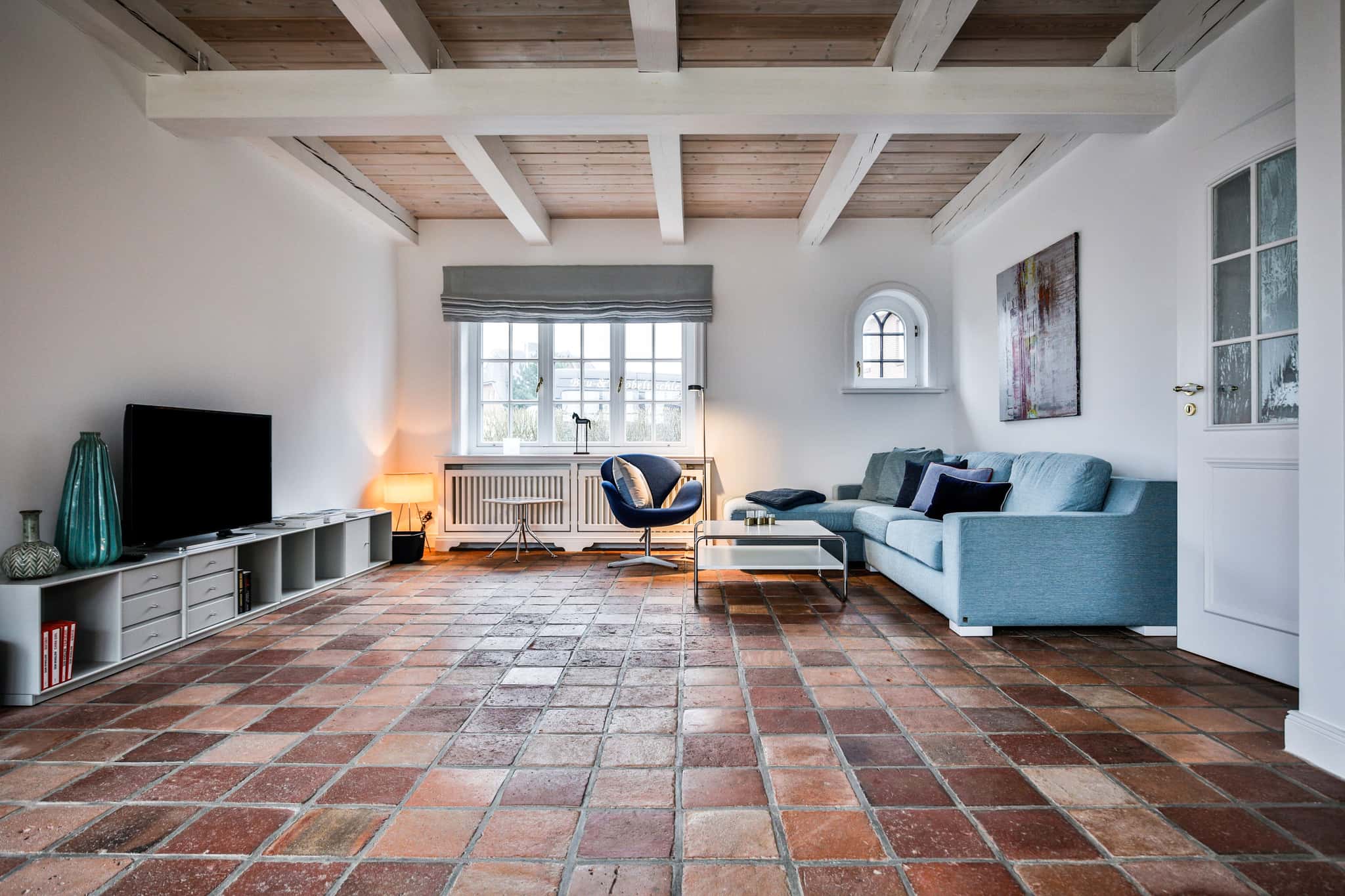 Wohnzimmer mit Fernseher auf Lowboard, hellblauem Sofa, blauem Sessel und Terrakottaboden, Haus Lochterbarig