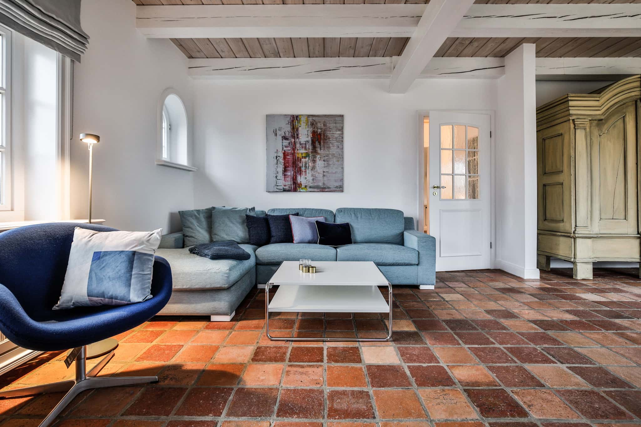 Wohnzimmer mit hellblauem Sofa, blauem Sessel und Terrakottaboden im Haus Lochterbarig