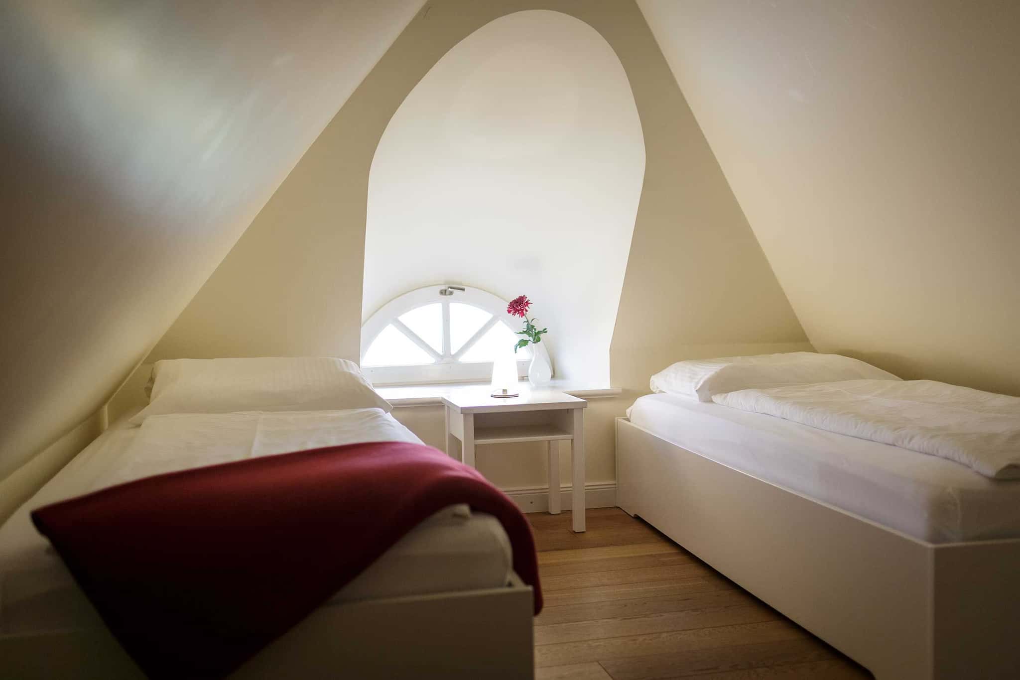Schlafzimmer mit zwei Einzelbetten unter der Dachschräge und Rundbogenfenster, Appartement Lüüvhoog
