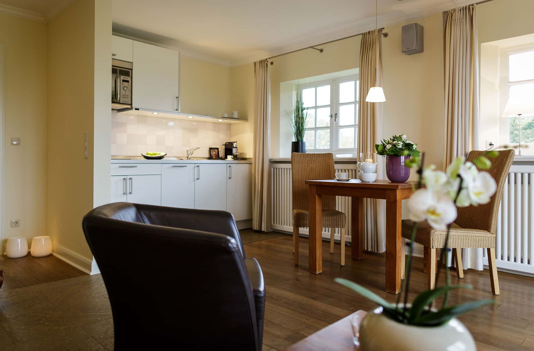Wohnküche mit weißer Küchenzeile, Esstisch mit Korbstühlen und Orchidee im Appartement Lüüvhoog