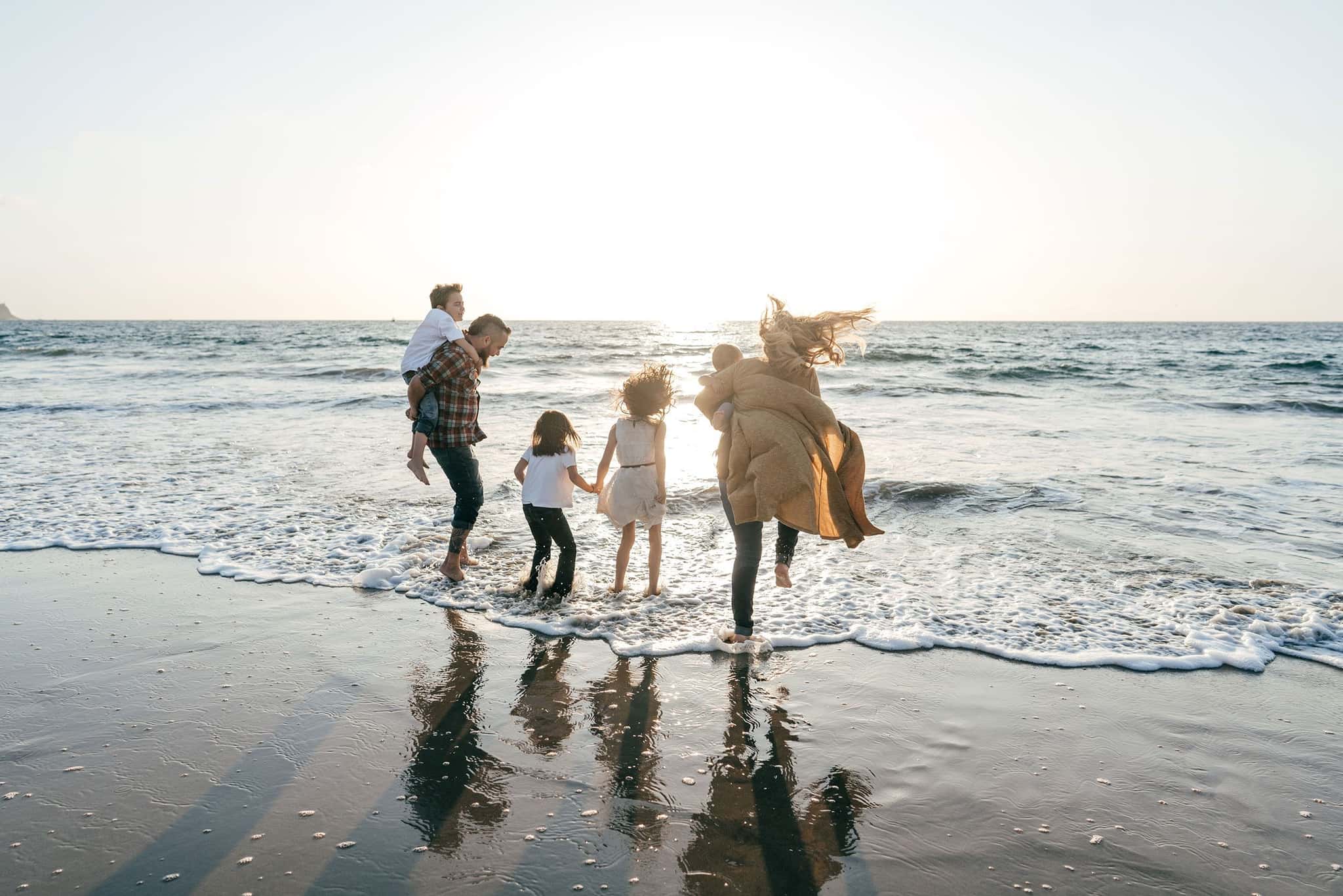 Familie mit Kindern spielt bei Sonnenuntergang in der Brandung am Strand