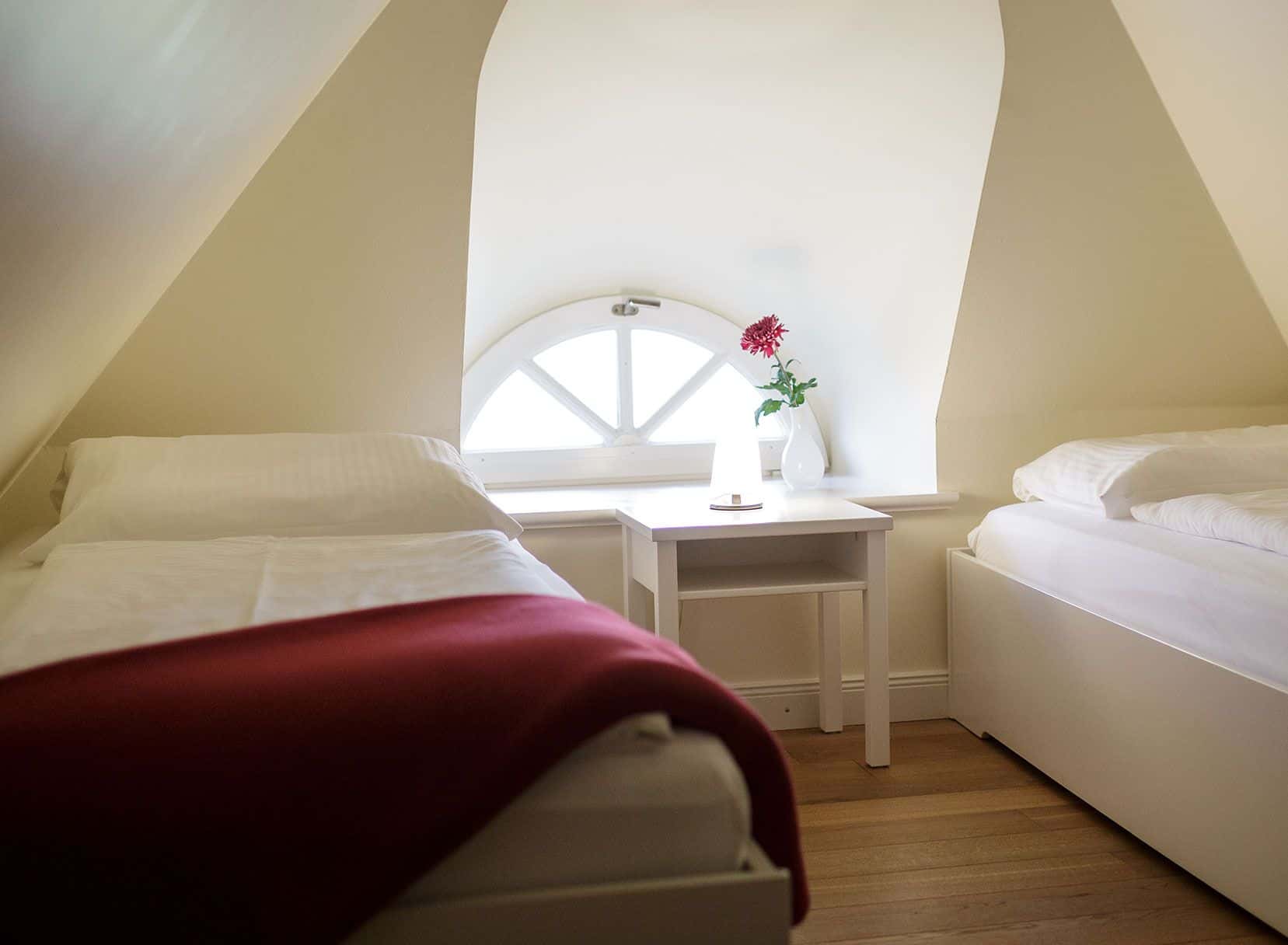 Schlafzimmer mit zwei Einzelbetten unter der Dachschräge und Rundbogenfenster, Appartement Lüüvhoog