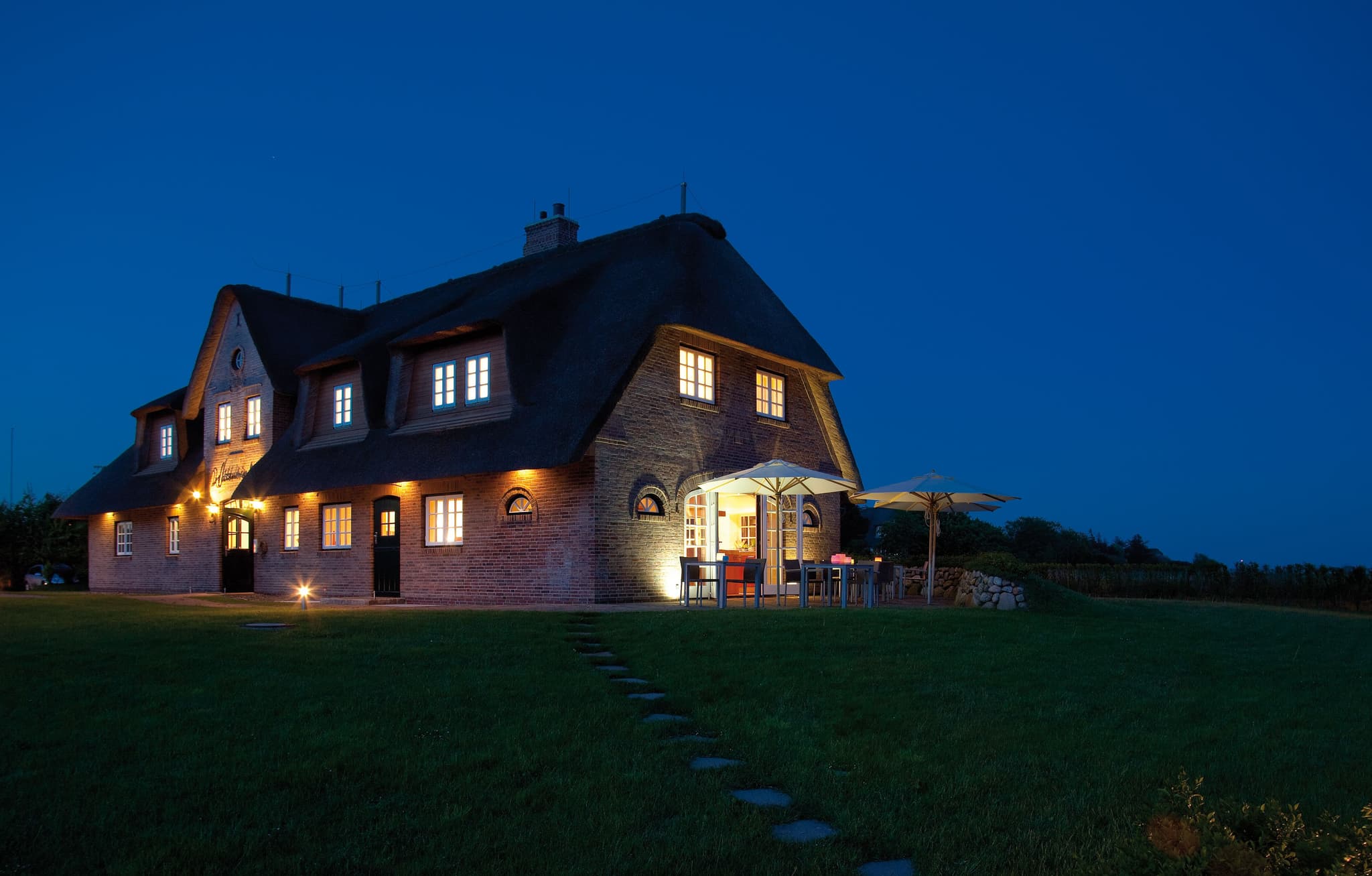 Reetgedecktes Backsteinhaus Lüüvhoog in der Dämmerung, beleuchtete Fenster, Terrasse und Rasen