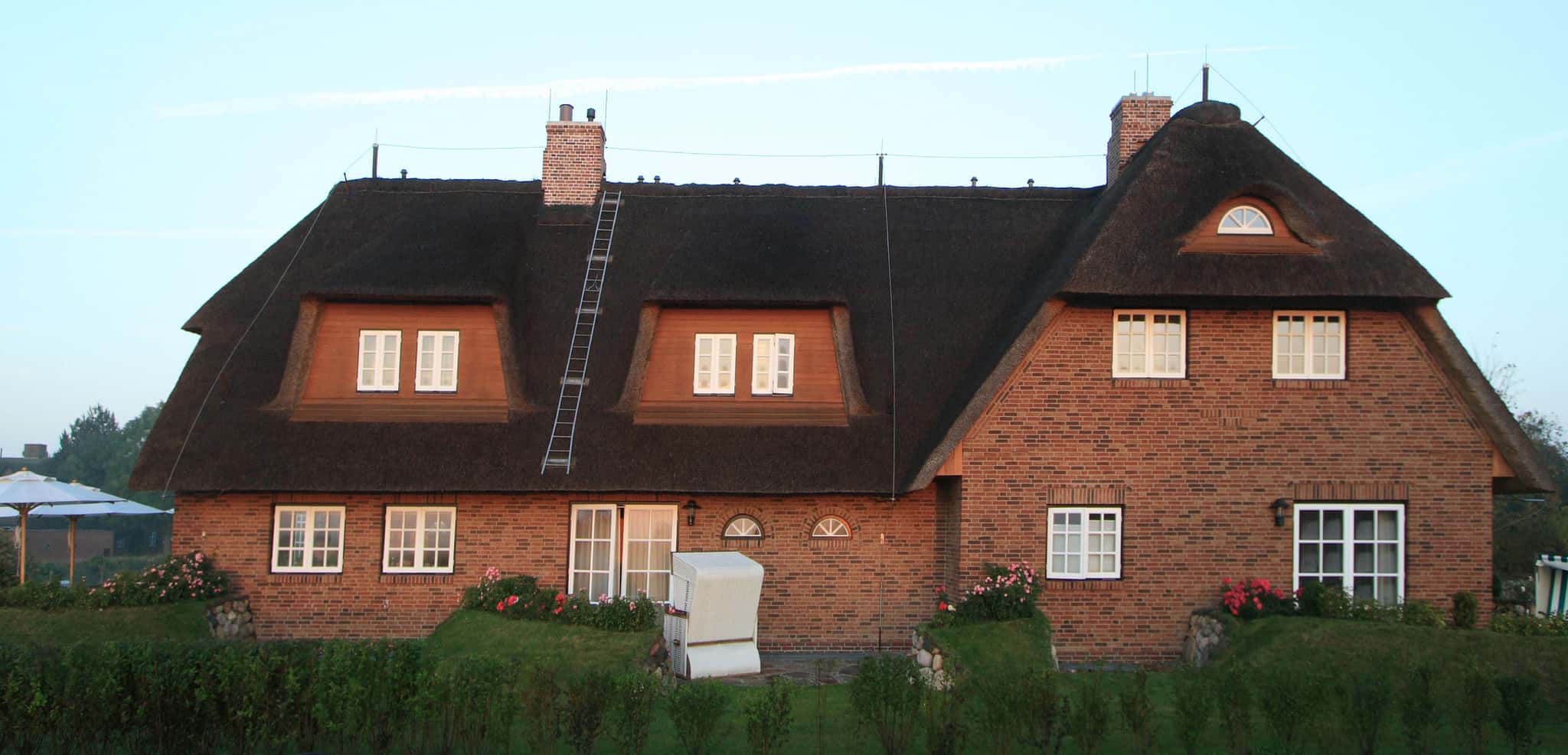Reetgedecktes Backsteinhaus Lüüvhoog, Frontansicht mit Gauben, Strandkorb und Hecke