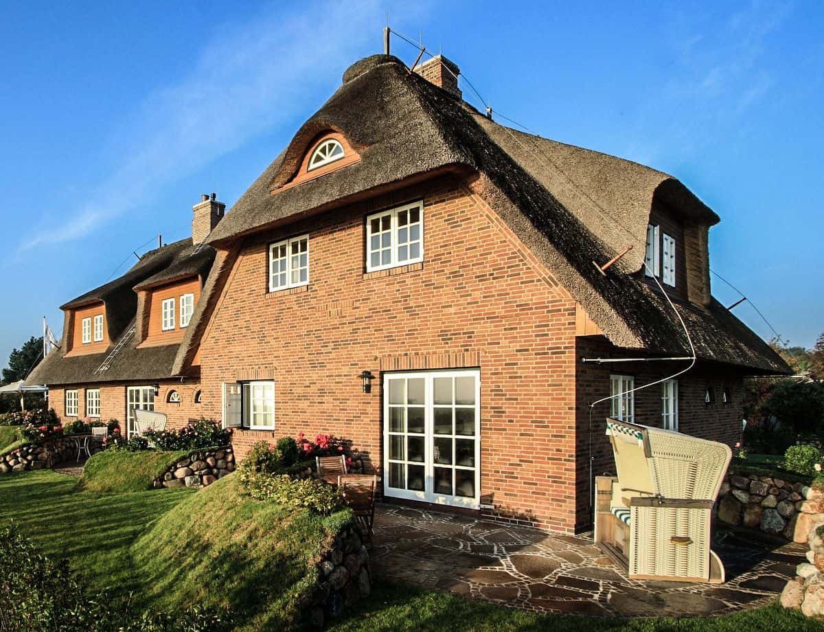 Reetgedecktes Backsteinhaus Lüüvhoog im Sonnenschein mit Steinterrasse und Strandkorb im Garten