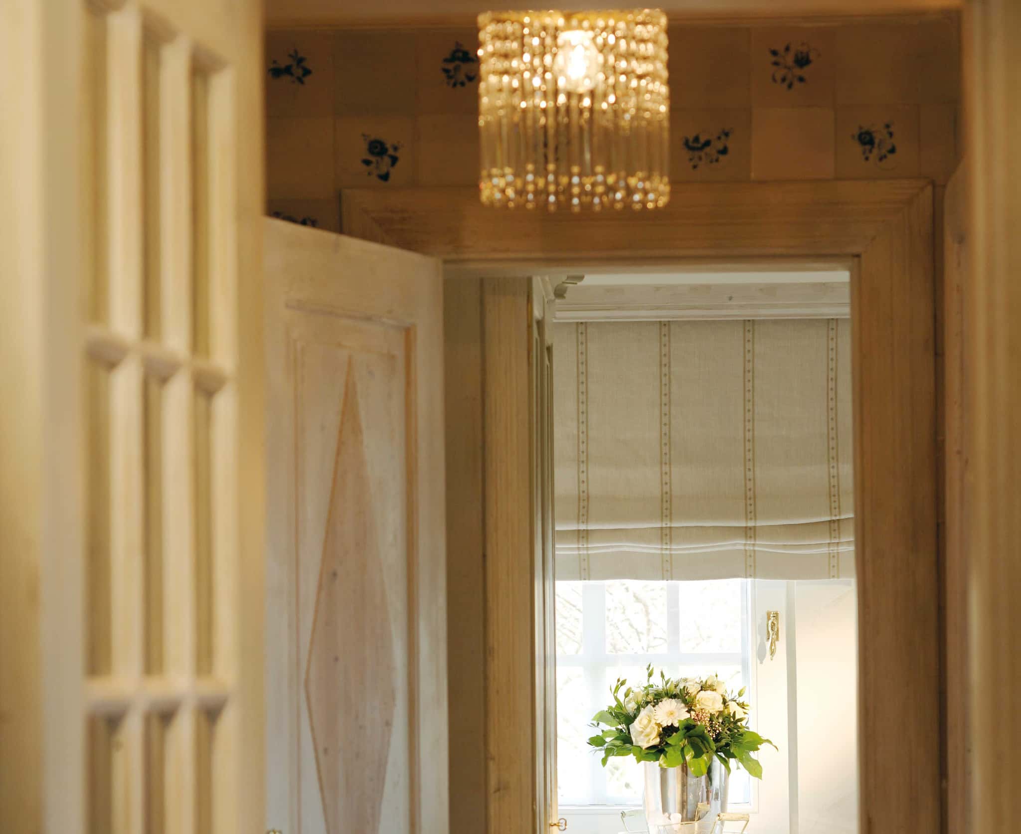 Blick durch die Tür auf Kristalllampe, Fliesen mit blauem Blumenmotiv und Fenster mit Blumenstrauß, Tipkenhoog