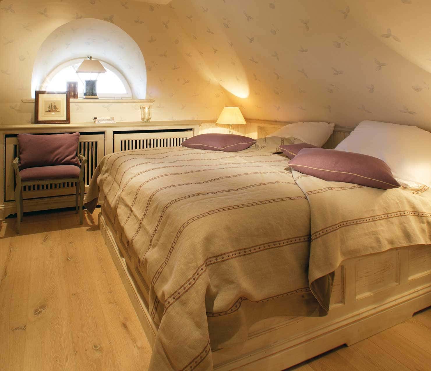 Schlafzimmer mit Doppelbett, Rundbogenfenster und Dachschräge in der Ferienwohnung Tipkenhoog